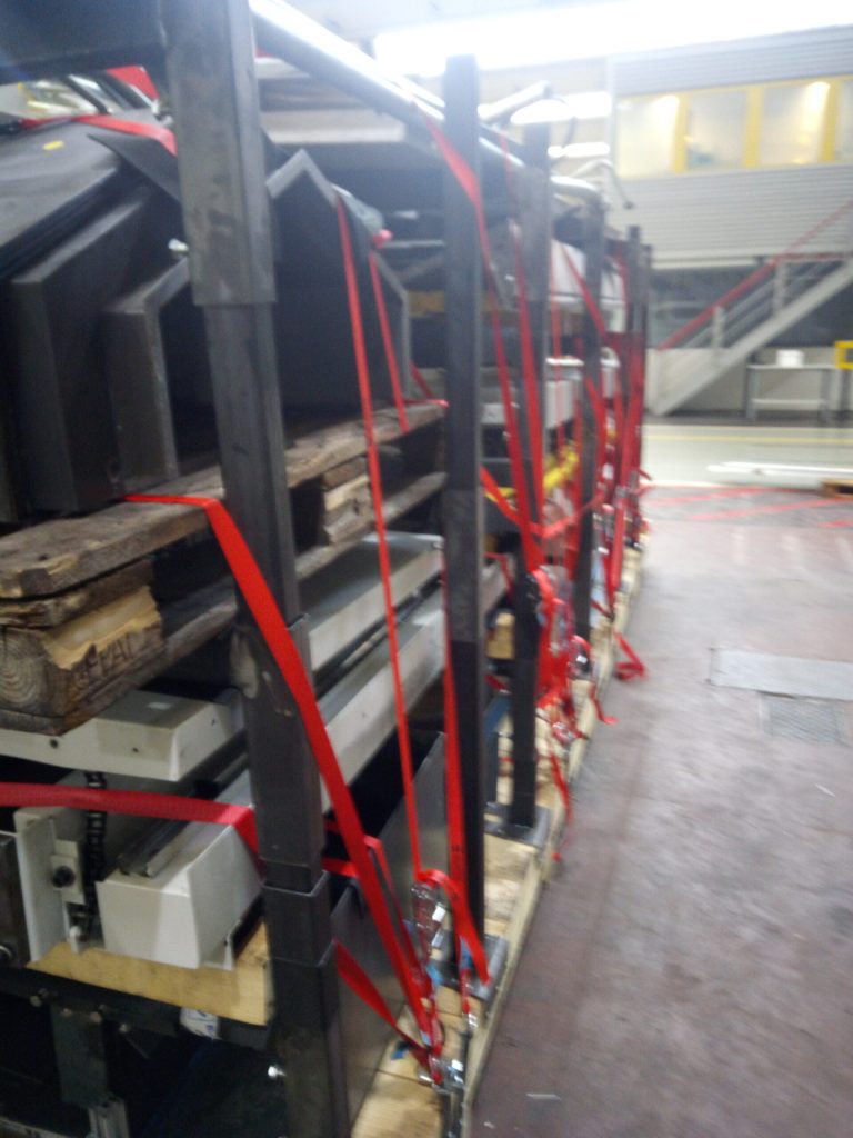 Rechte Seite einer Transportpalette mit befestigten Maschinenbauteilen und roten Spannbändern